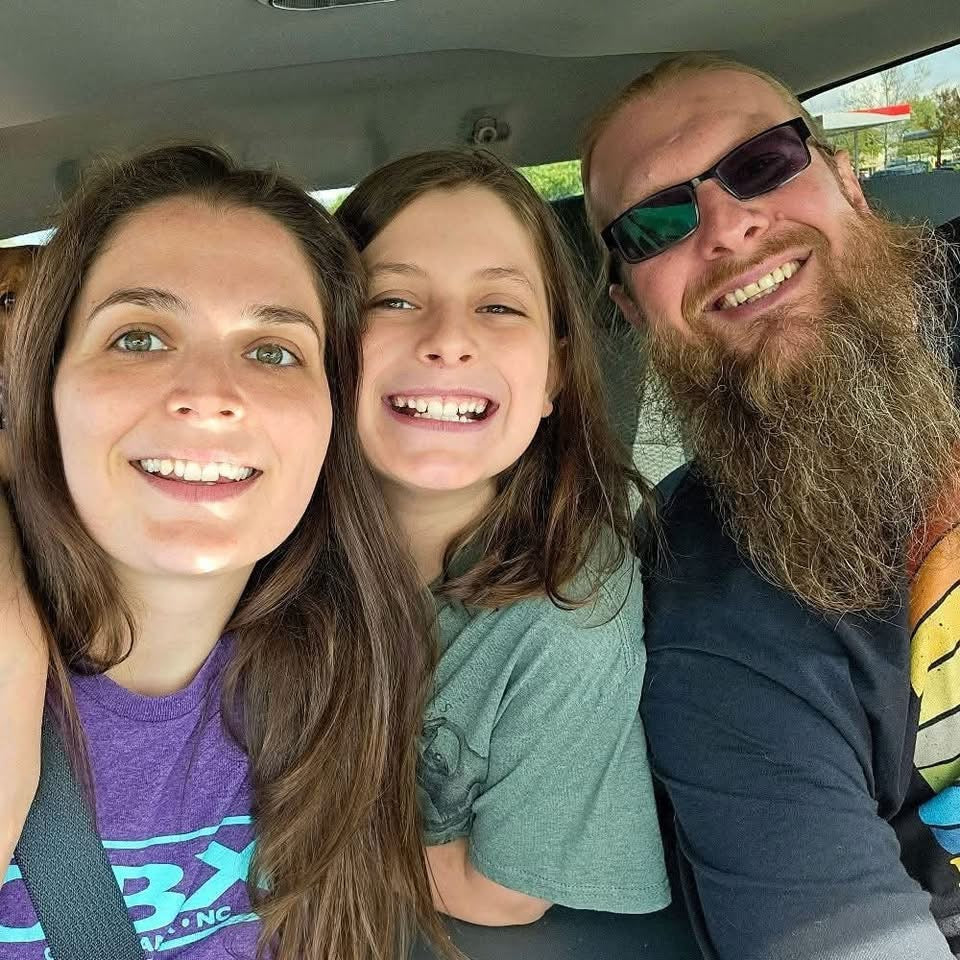 Three people sitting inside a vehicle, smiling at the camera.
