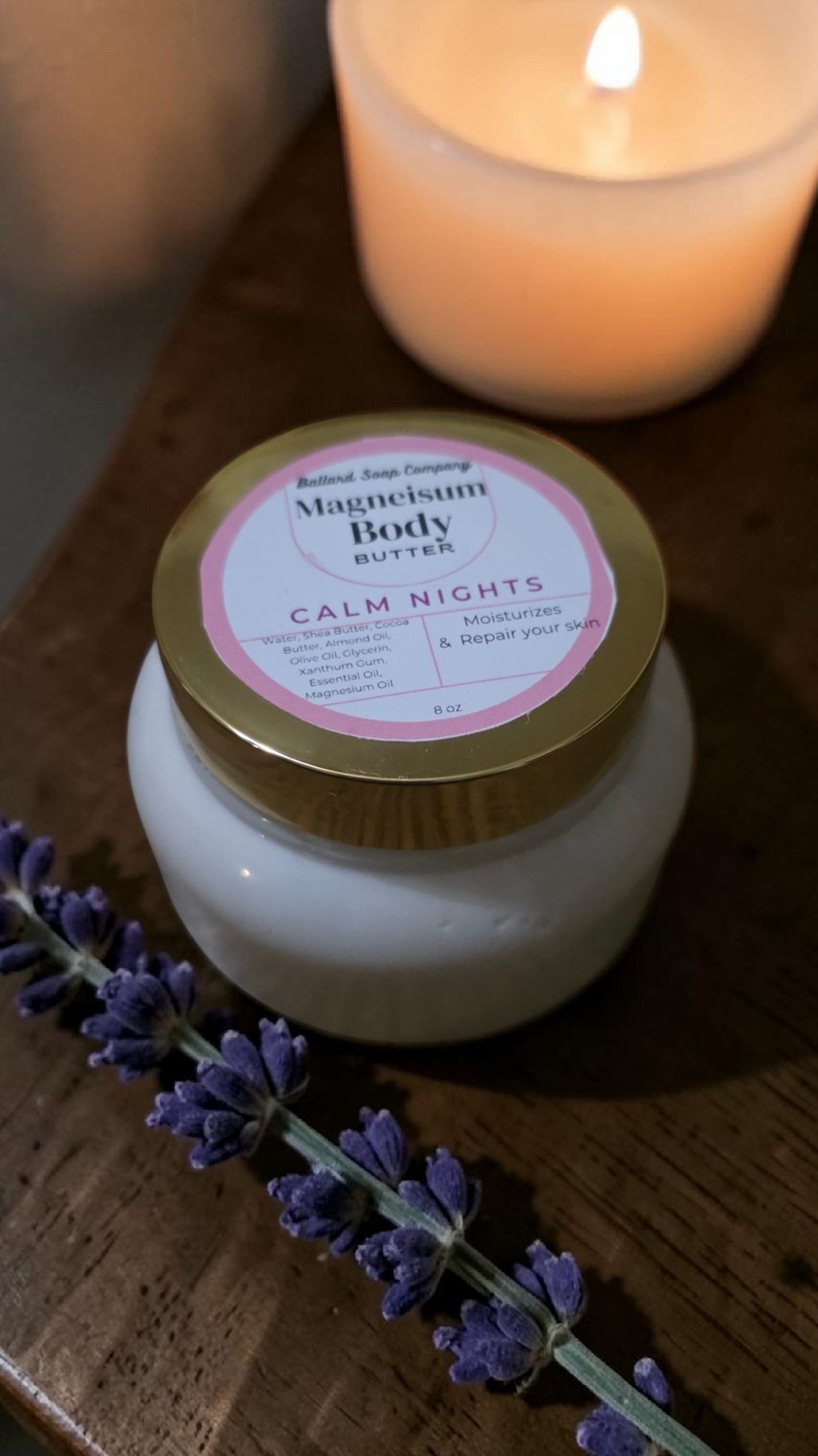 Jar of magnesium body butter with a lavender flower and lit candle on a wooden surface
